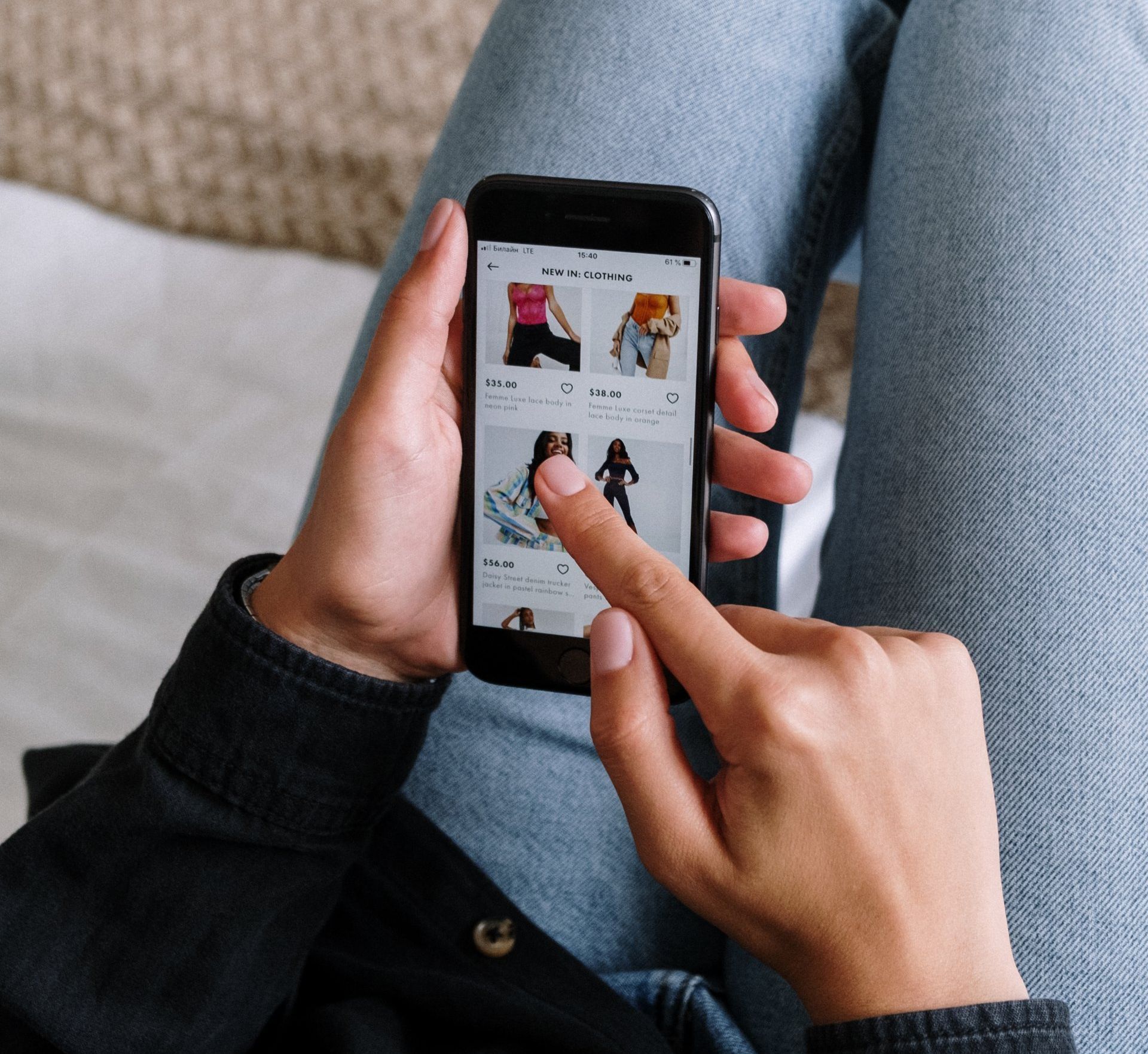 Hands using a smartphone to browse a clothing shopping app on a couch