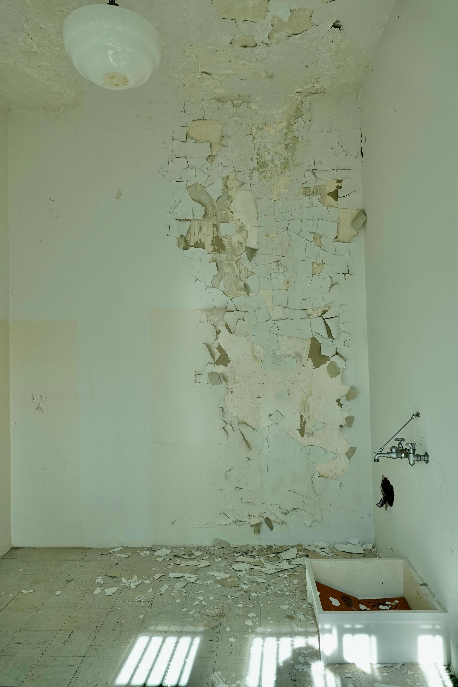 Dilapidated room with peeling wall paint, damaged ceiling, and sunlight on the floor
