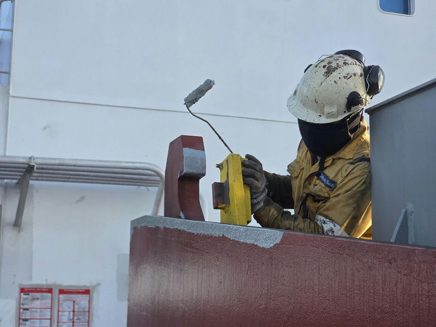 Construction worker painting a red wall with a roller on a rooftop, wearing a helmet and mask.