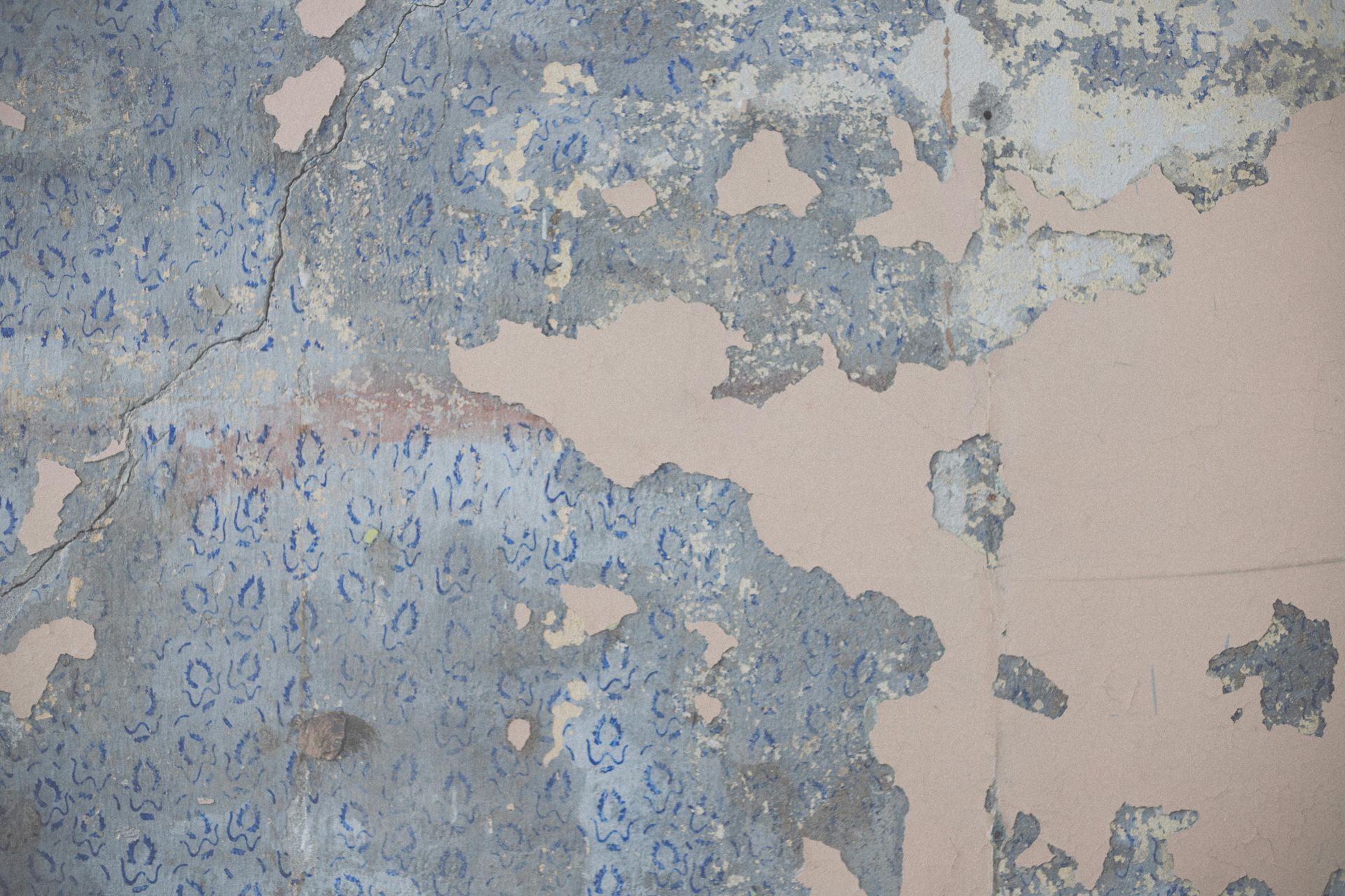 Peeling blue and gray paint on a worn wall with exposed pink plaster.