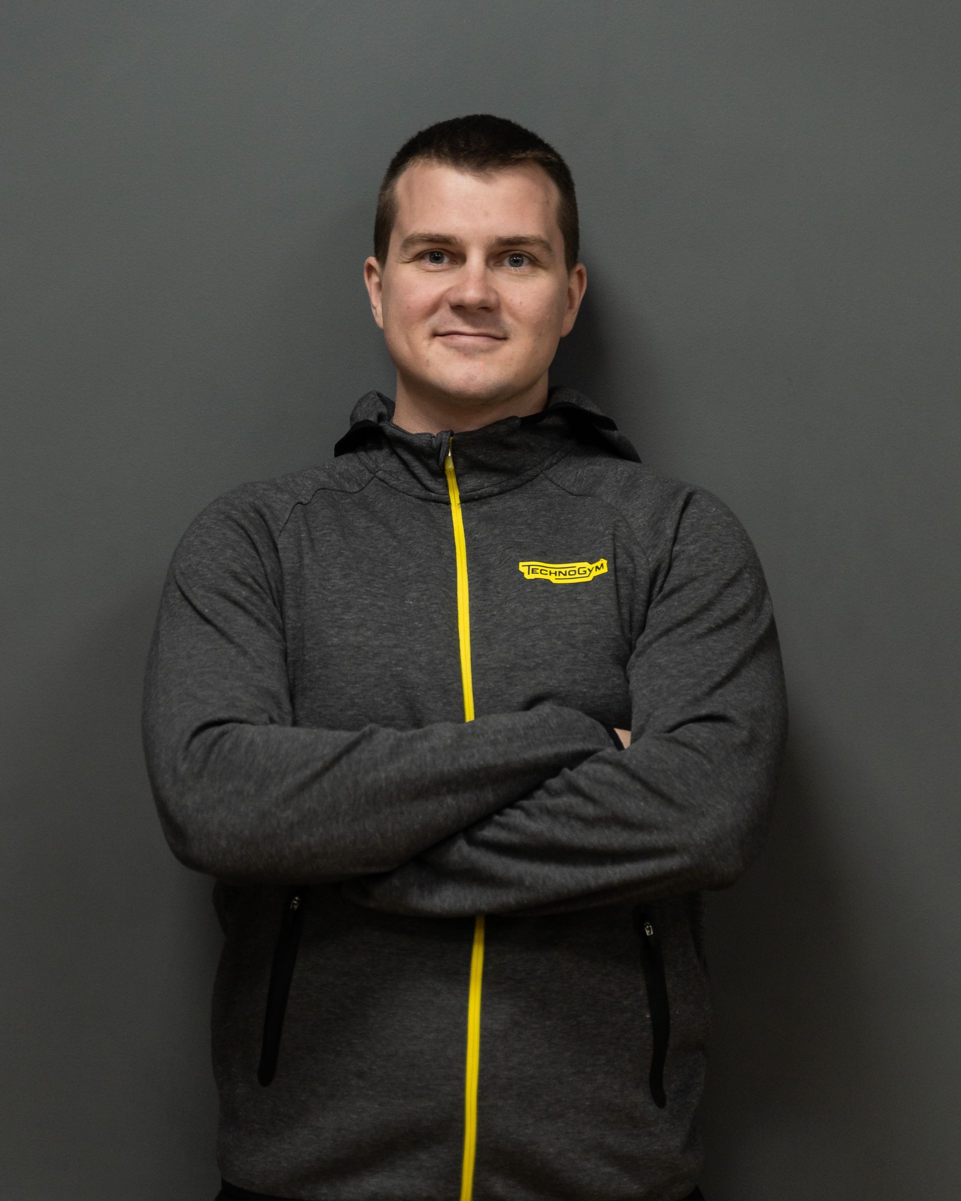 a man wearing a grey jacket with a yellow zipper has his arms crossed