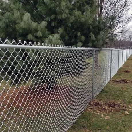 Black metal fence with concrete base beside a building and dirt path in sunlight