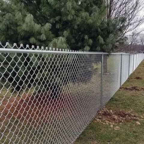 Black metal fence with concrete base beside a building and dirt path in sunlight