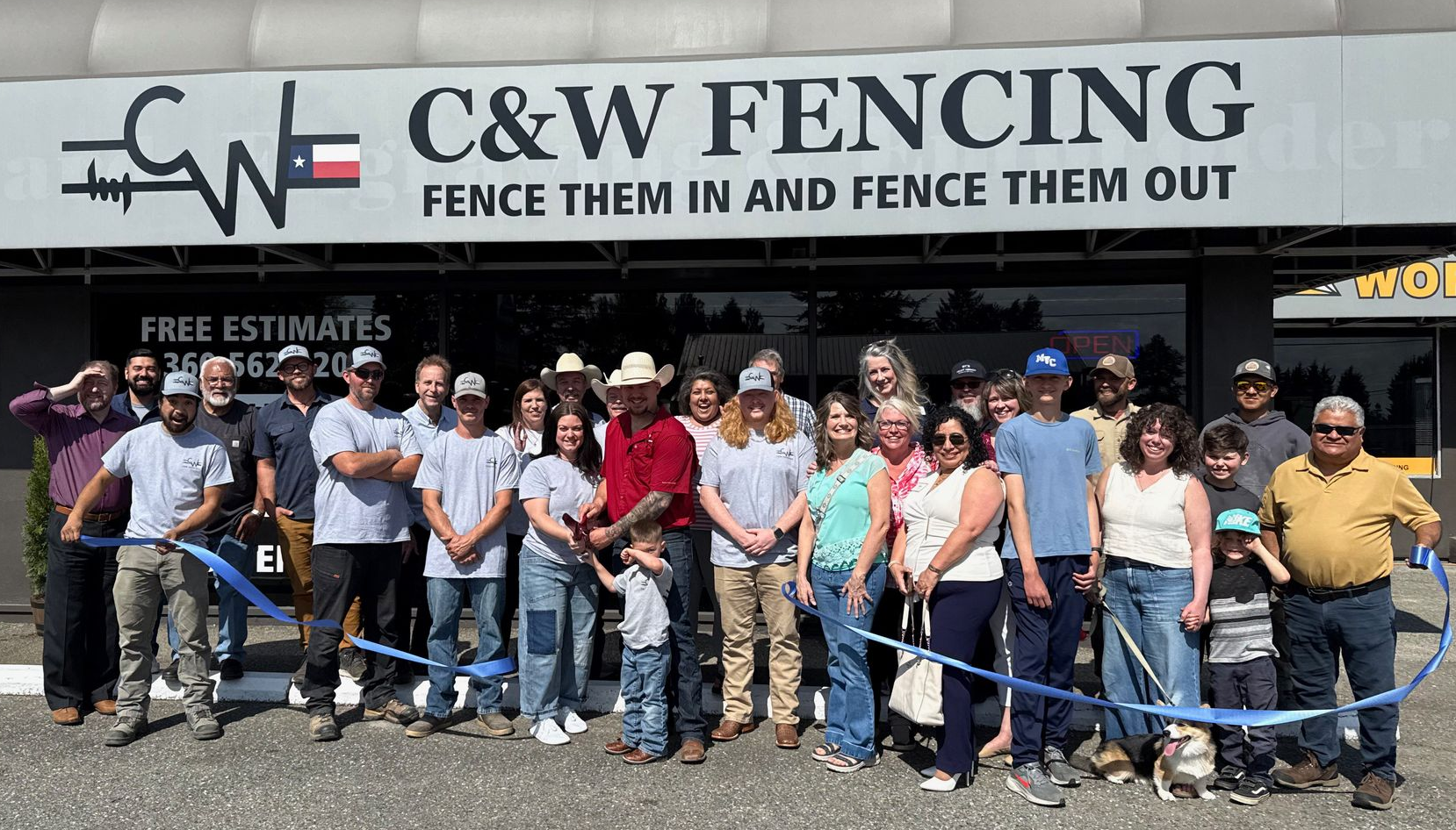 Group of people posing outside C&W Fencing storefront with a “Free Estimates” sign and fencing equipment.