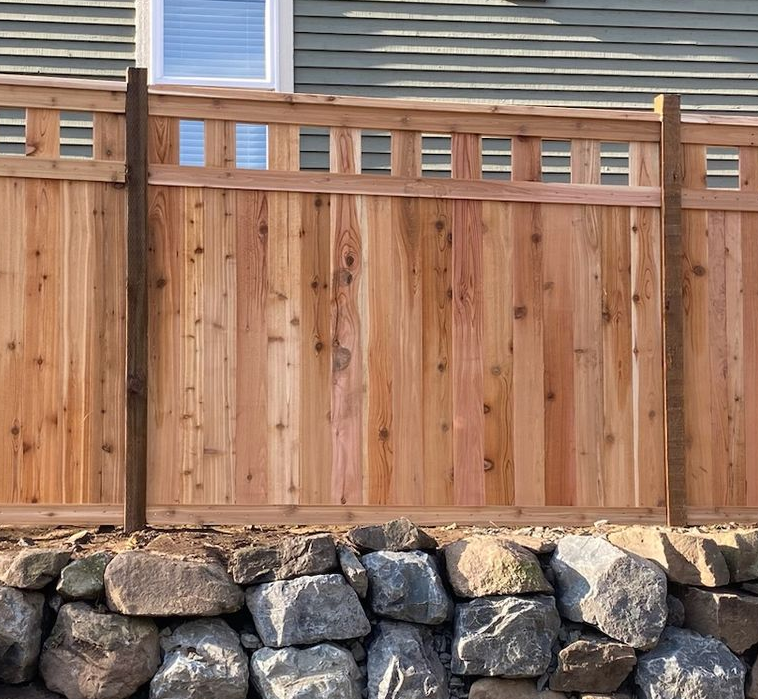 Wooden backyard fence with stone base beneath a house window and siding