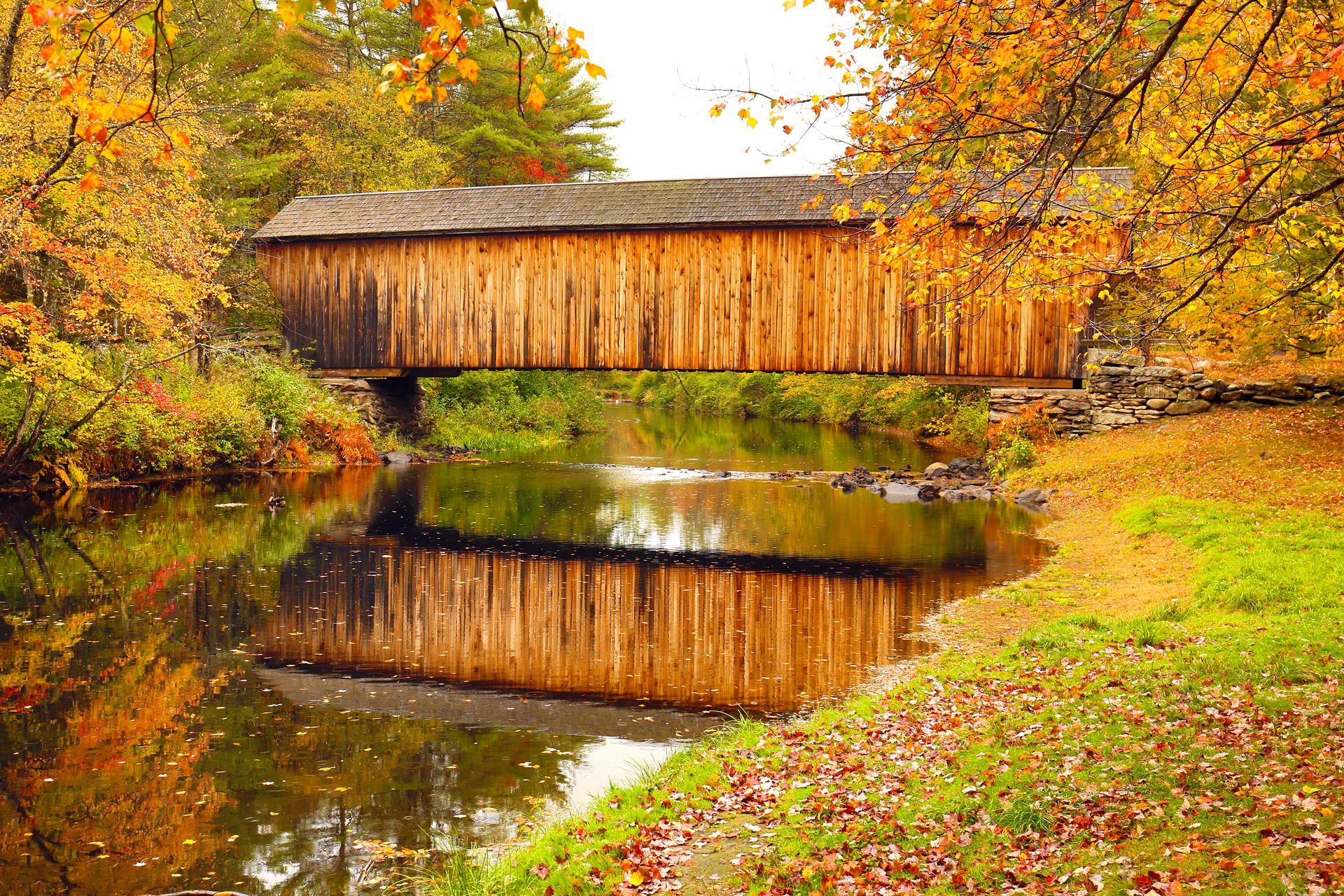 A wooden covered bridge over a river in autumn