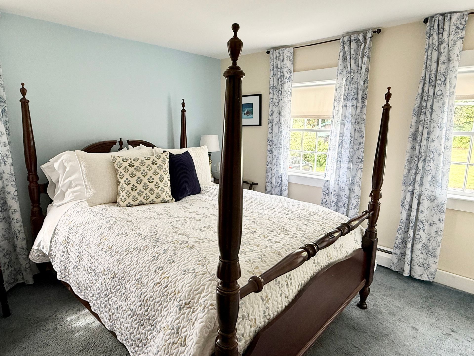 Bright bedroom with a four-poster bed, patterned bedding, and large windows with floral curtains.