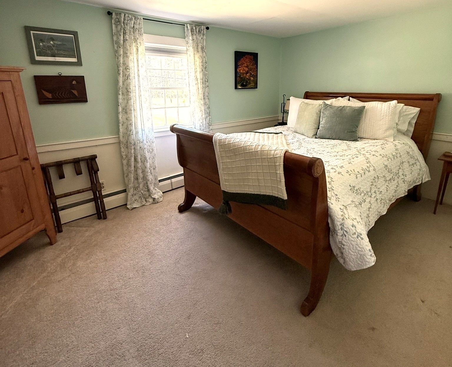 Bright bedroom with a wooden bed, light blue walls, beige carpet, and a window with curtains.