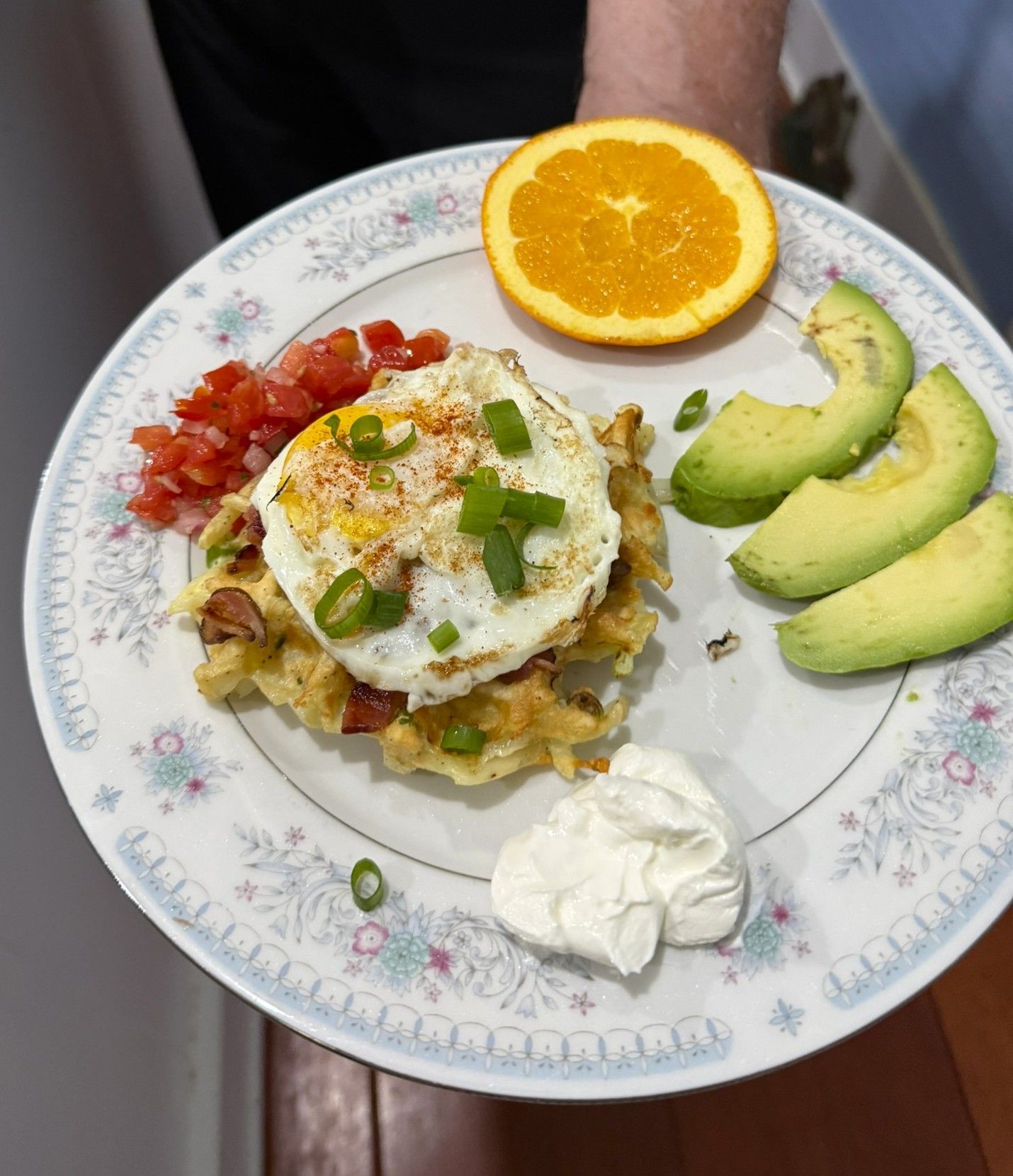 Plate with a topped breakfast dish, avocado slices, orange half, salsa, and a dollop of sour cream.