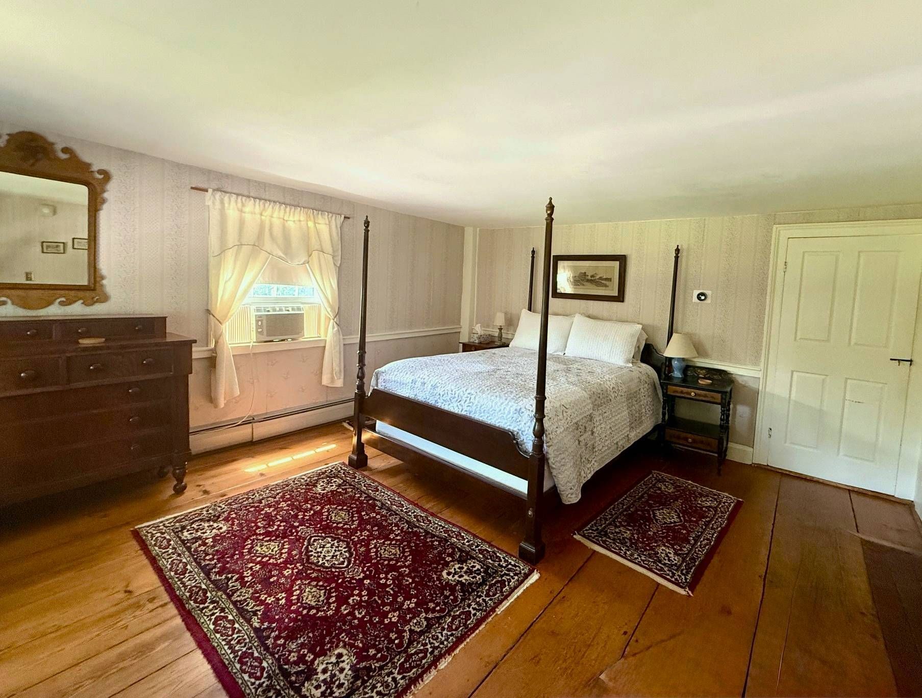 A bedroom with a four poster bed , dresser , mirror and rug.
