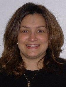 A woman with long brown hair and a necklace is smiling for the camera.