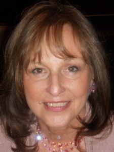 A woman wearing a pink sweater and a pink necklace is smiling for the camera.