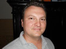 A man in a grey shirt is smiling for the camera.