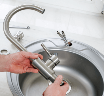 A person is fixing a faucet in a kitchen sink