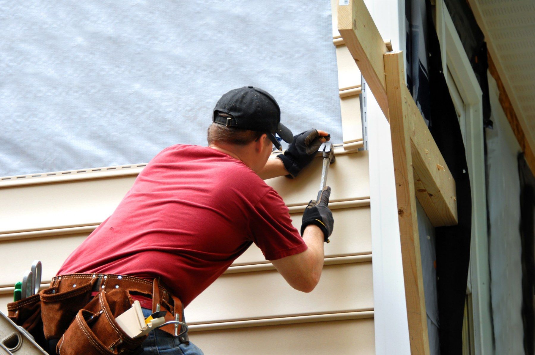 A man is installing siding on the side of a house.