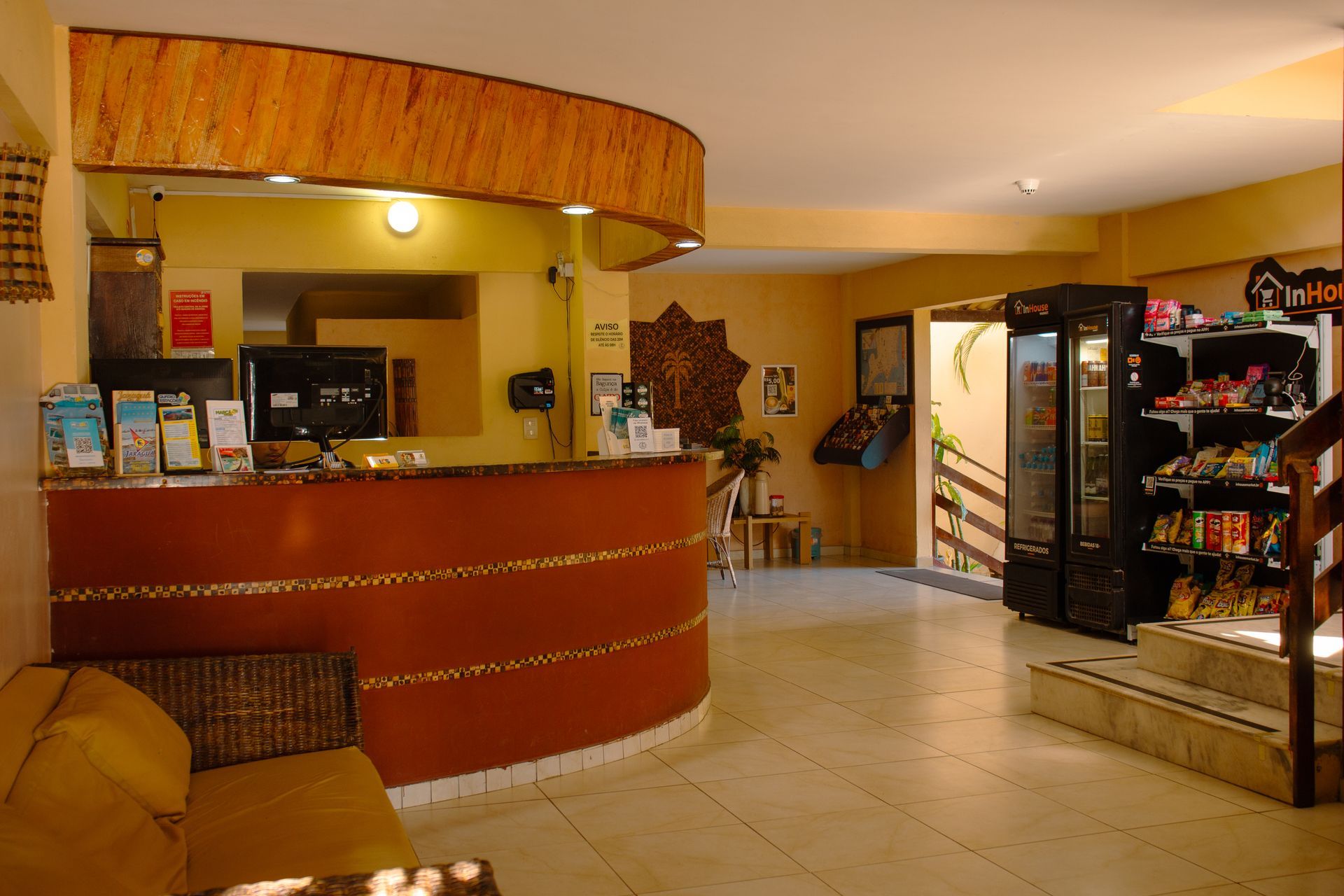 Hall de entrada vazio do hotel com balcão de recepção vermelho, piso de azulejo e prateleiras de exposição.
