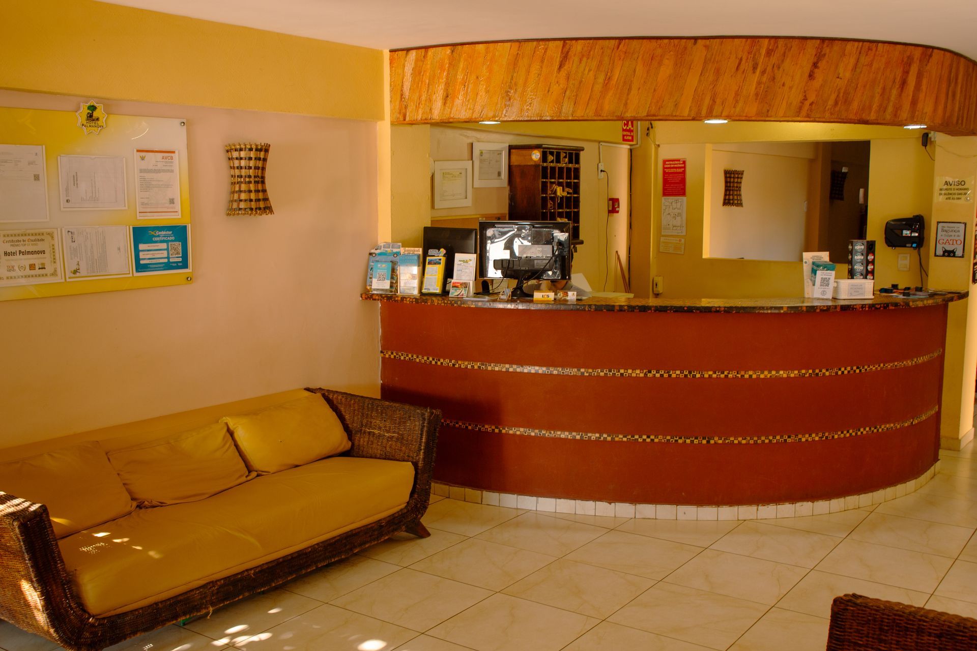 Hall de entrada com balcão de recepção curvo vermelho, paredes bege e um sofá na área de espera.