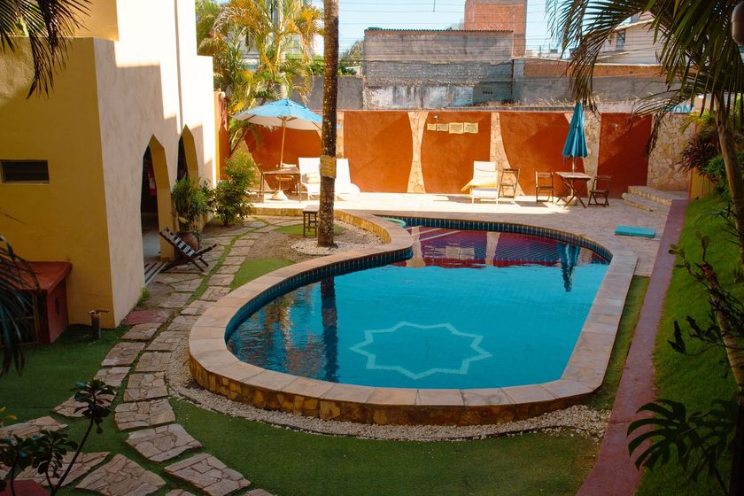 Pequena piscina no quintal com pátio, espreguiçadeiras e paredes bege, banhada por sol.