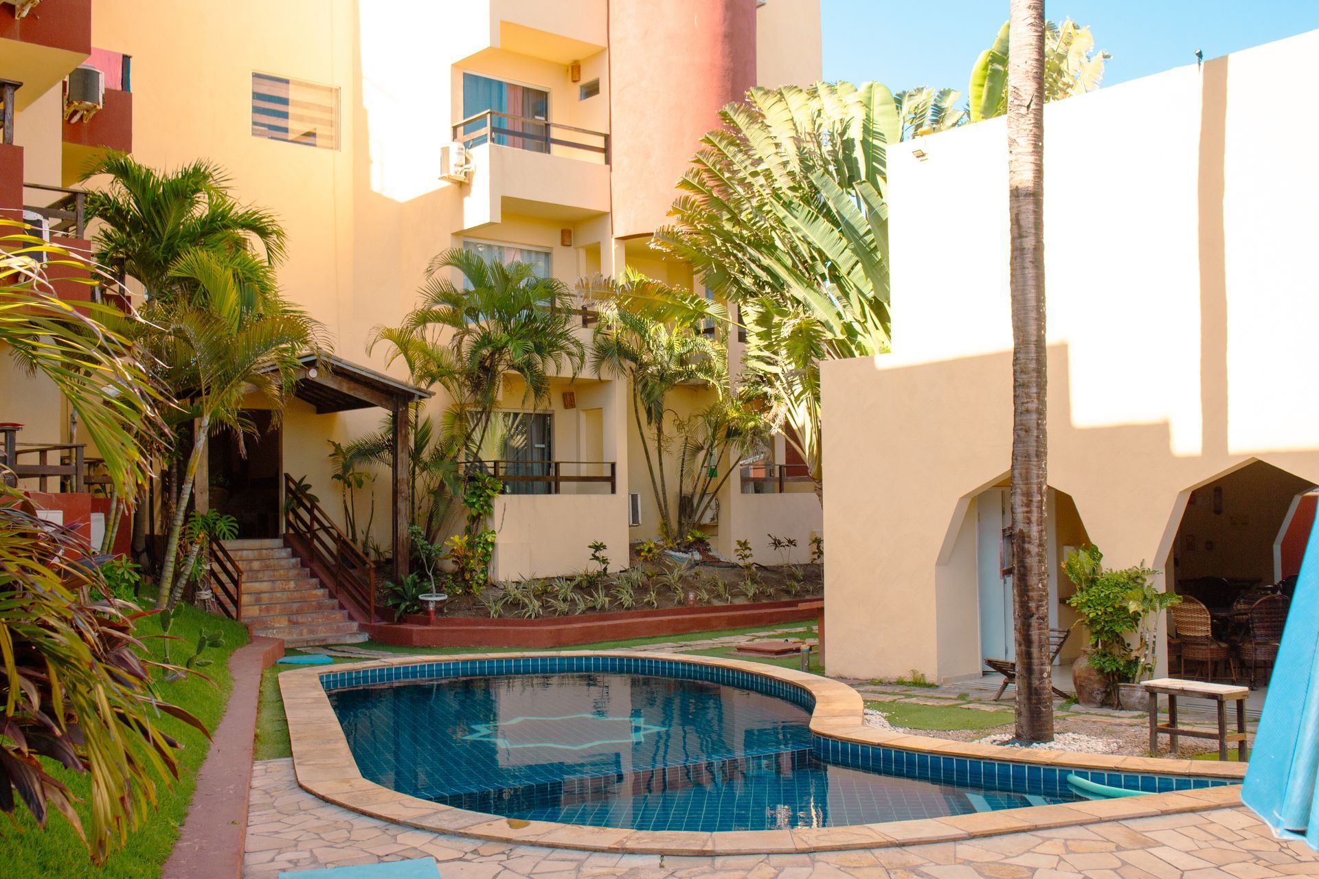 Piscina no pátio rodeada por plantas tropicais e prédios de apartamentos cor de pêssego.