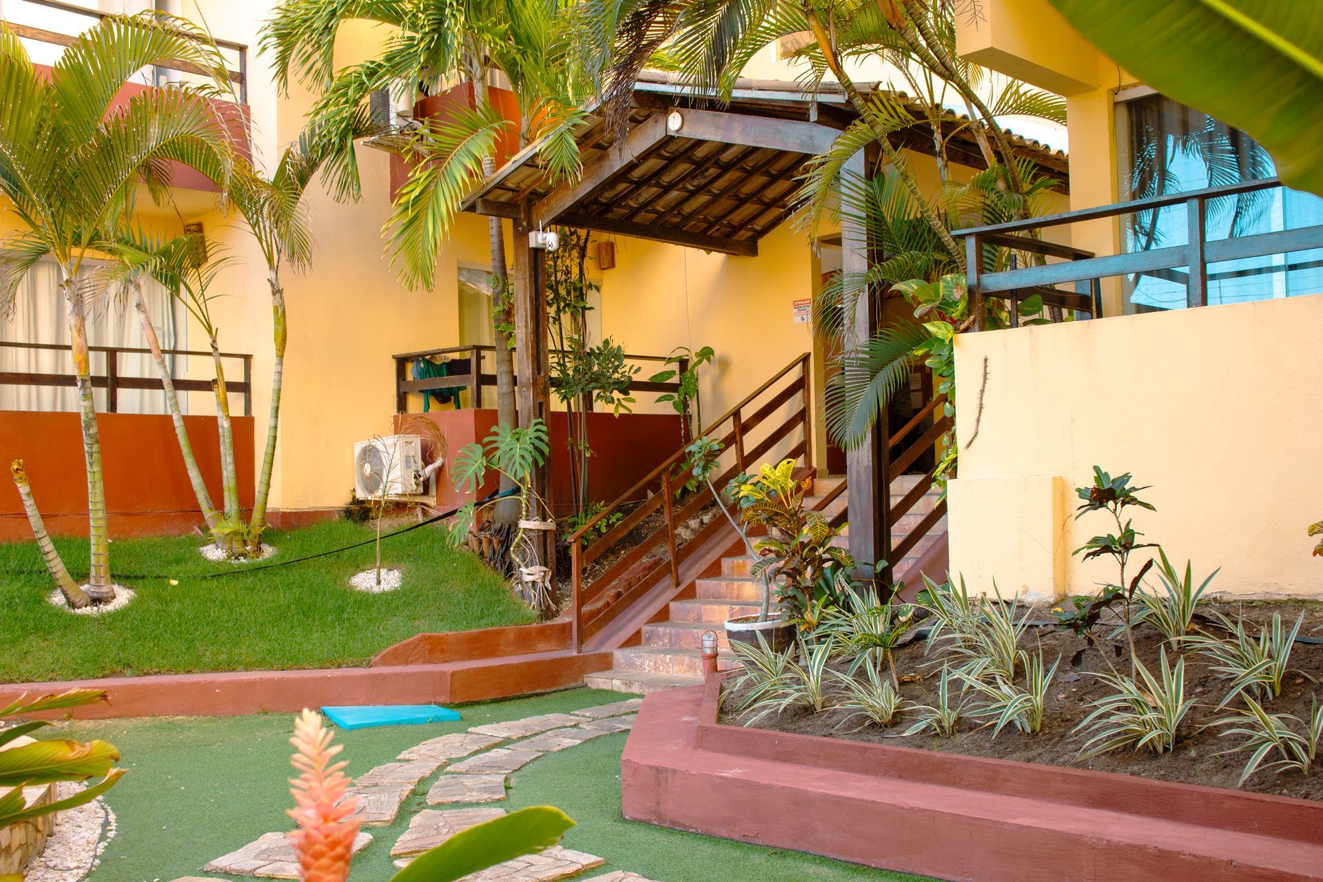 Pátio de apartamento tropical com palmeiras, escadas e paisagismo.