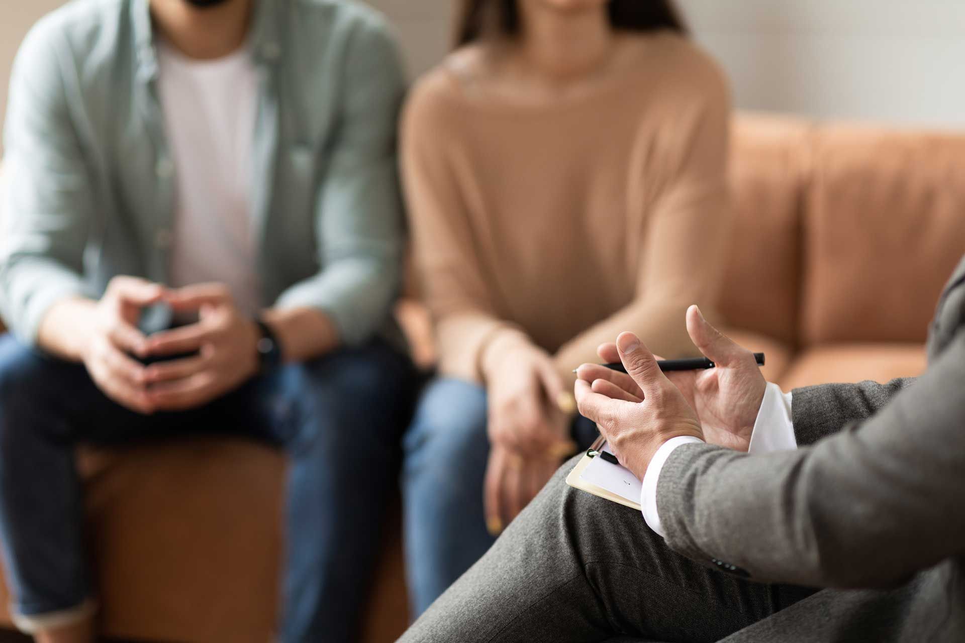 A man and a woman are sitting on a couch talking to a counselor.