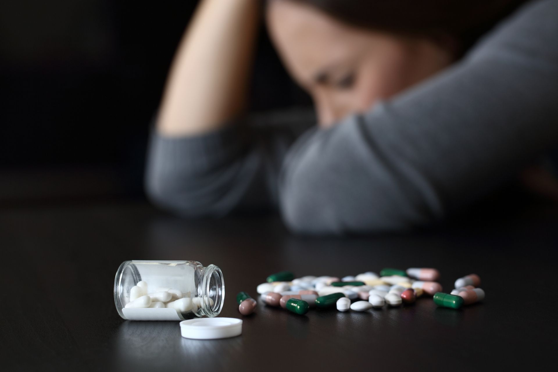 A woman is sitting at a table with a jar of pills on it.
