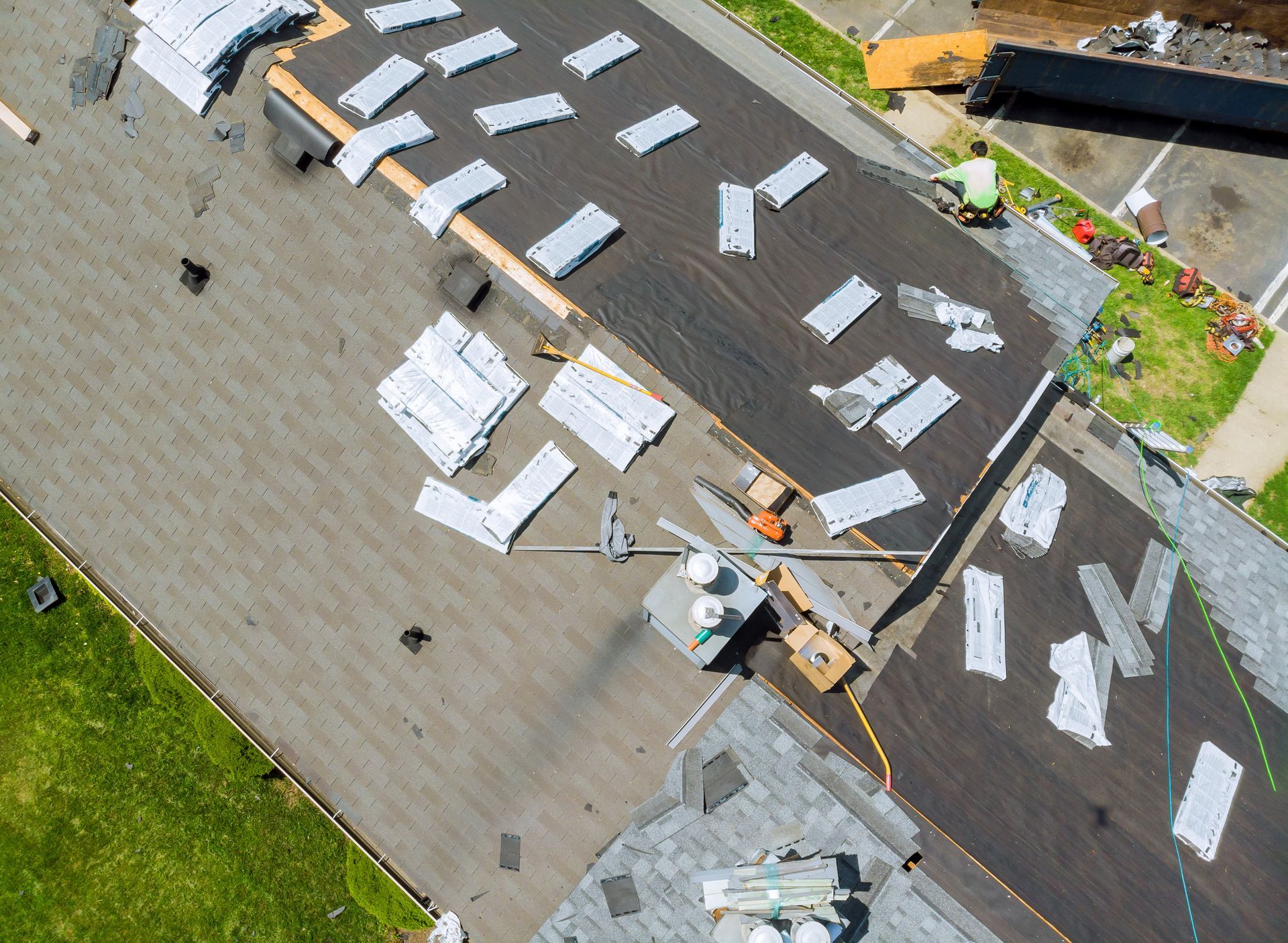 Aerial view of a roof being repaired, with workers, tools, and stacked shingles scattered across the surface.