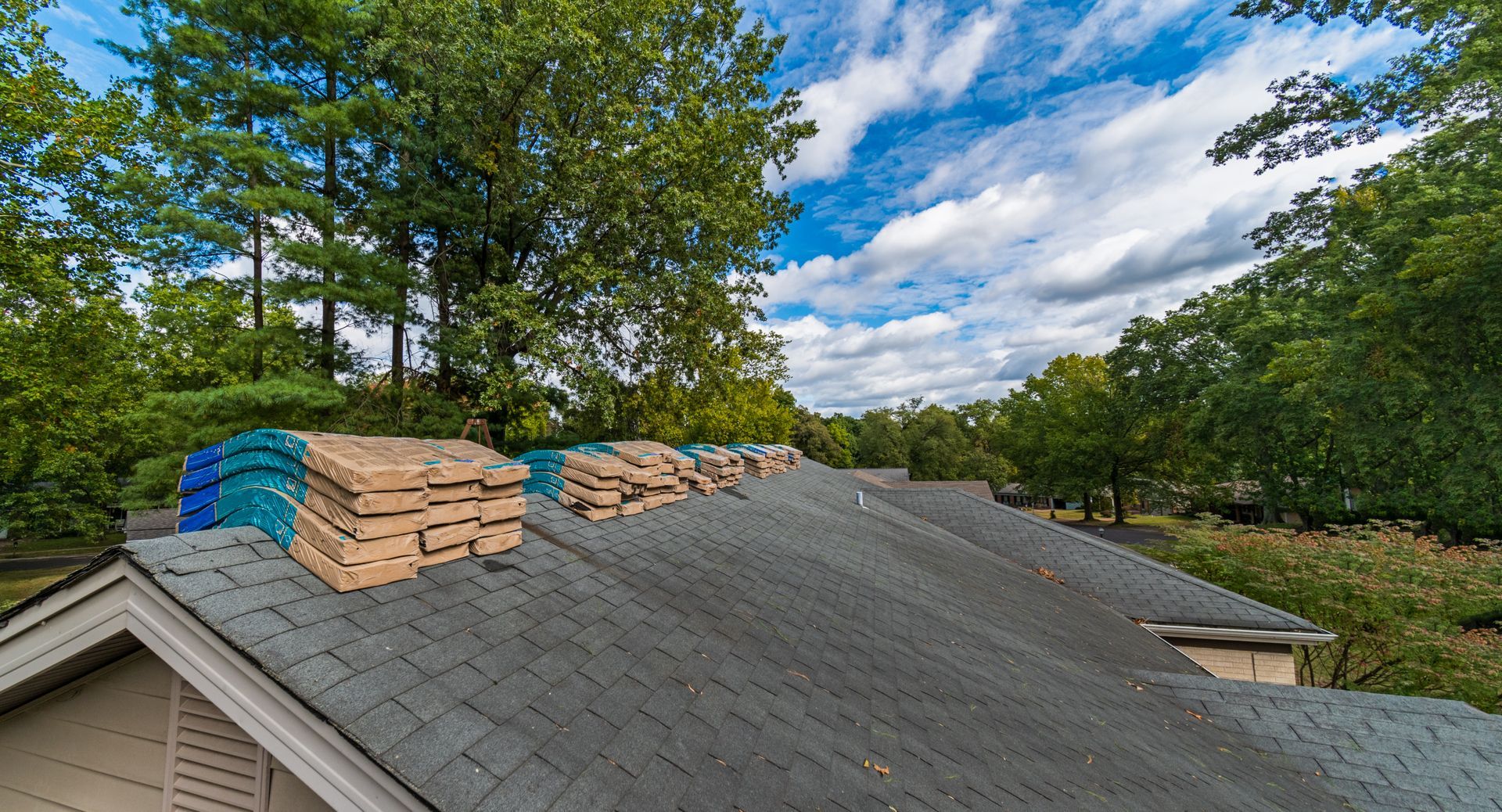Roof covered with sandbags and blue tarps under a cloudy sky, with trees in the background