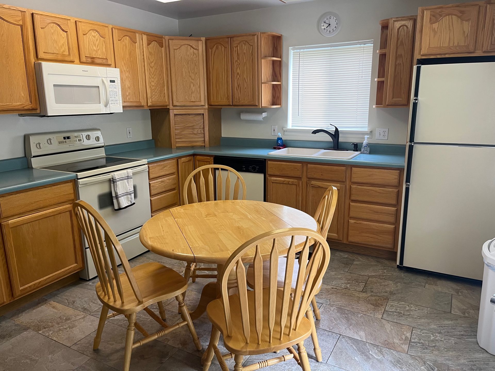Kitchen with wooden cabinets, table and chairs, appliances, and a window.