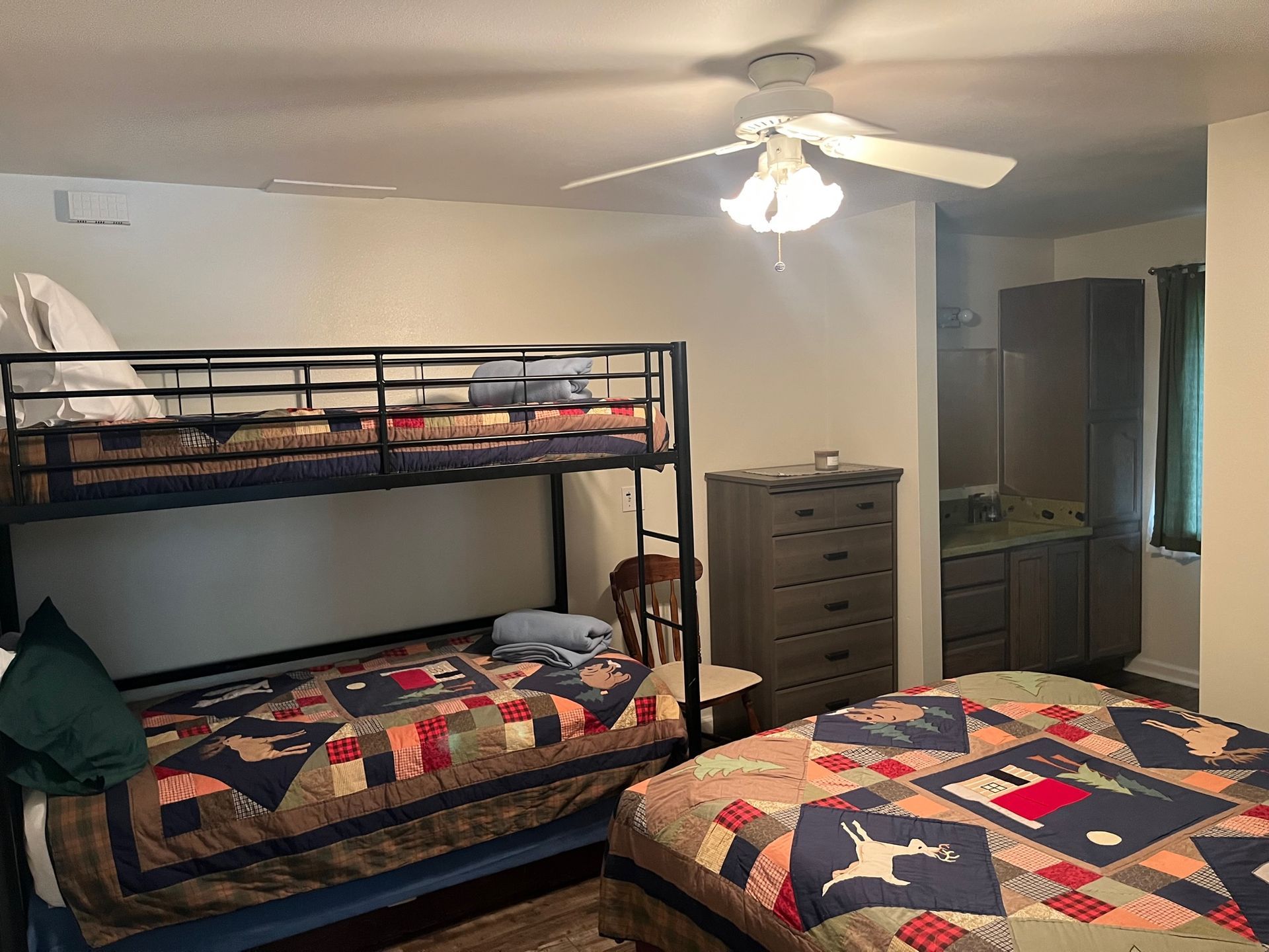 Bedroom with bunk beds, double bed, dresser, vanity, and ceiling fan.