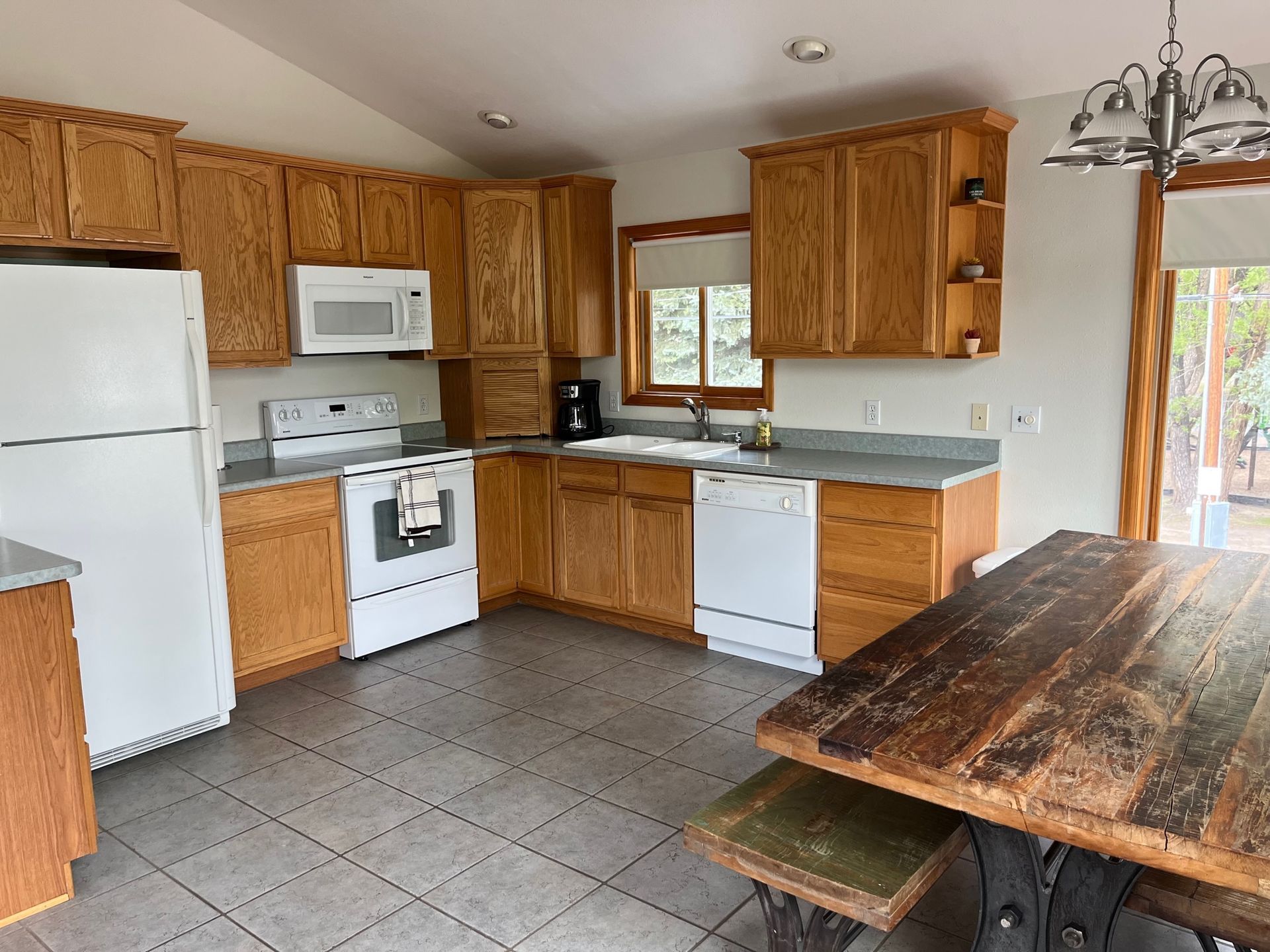 Kitchen with wooden cabinets, white appliances, gray countertops, and a rustic dining table.