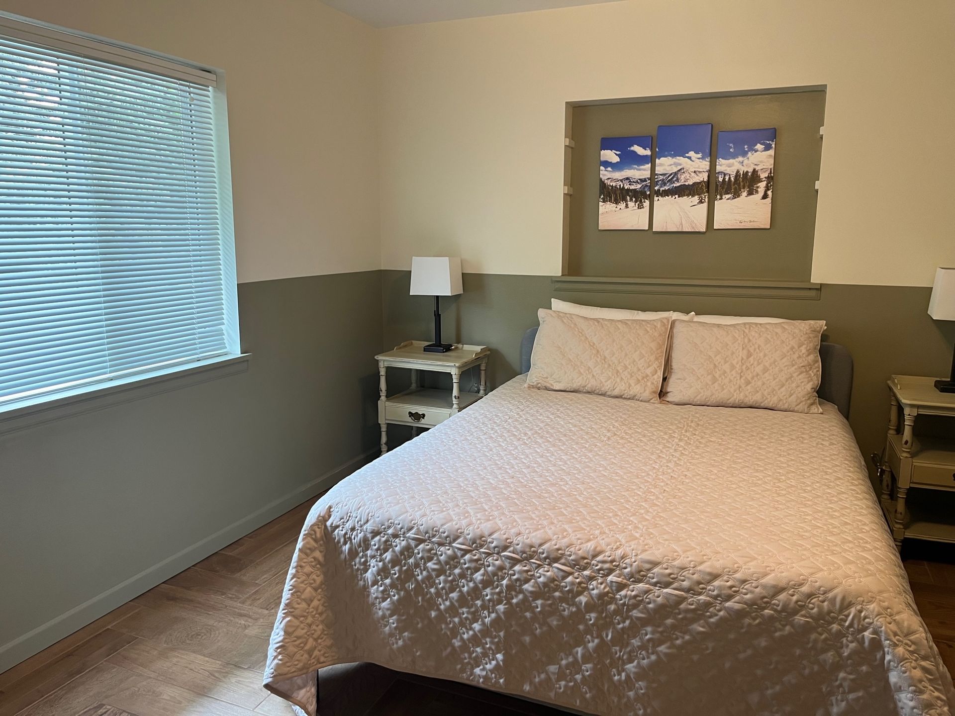 Bedroom with a bed, nightstands, window, and mountain art. Two-tone walls, beige and green.