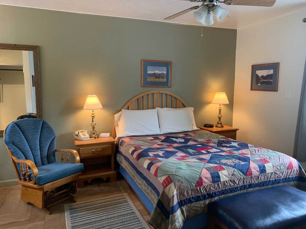 Bedroom with a blue chair, a bed with a quilt, two nightstands, and a mirror.