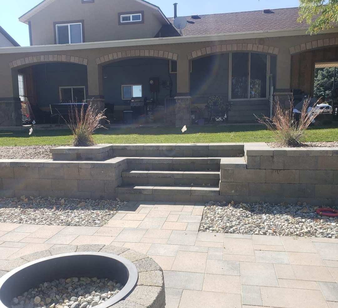 A stone stairway and retaining wall lead up to a house with a porch. A fire pit sits in the foreground.
