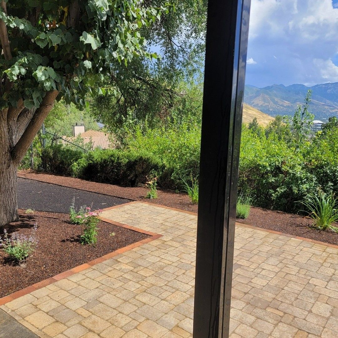 View of paved patio with surrounding landscape of trees, bushes, and mountains.
