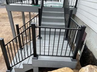 Stairs with gray treads and black railings leading up to a deck area, exterior shot.