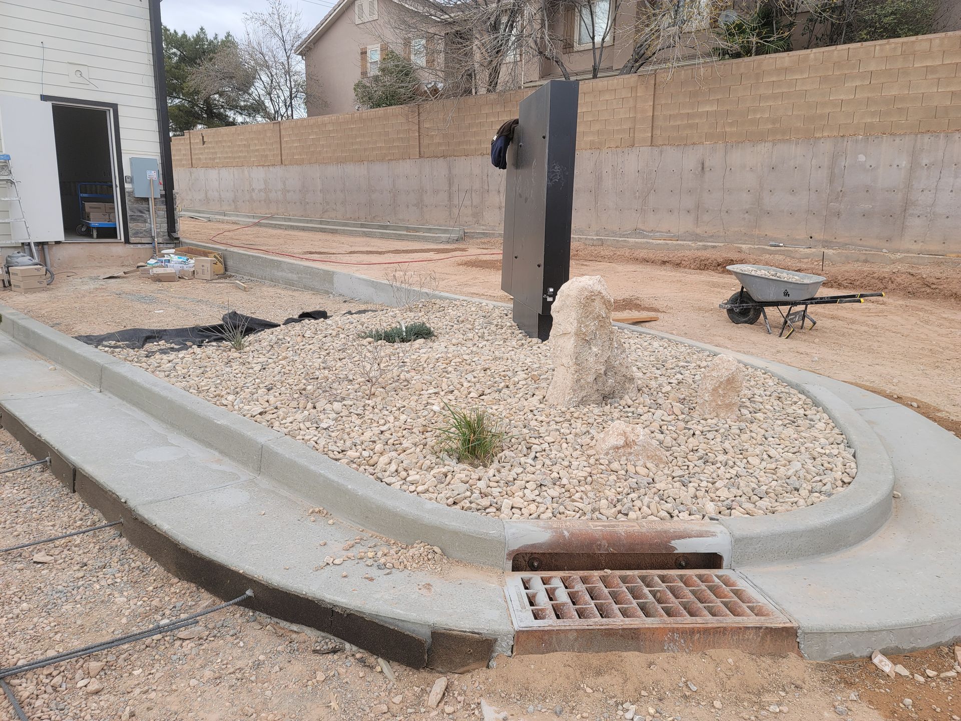 A concrete curb is surrounded by gravel and a wheelbarrow.