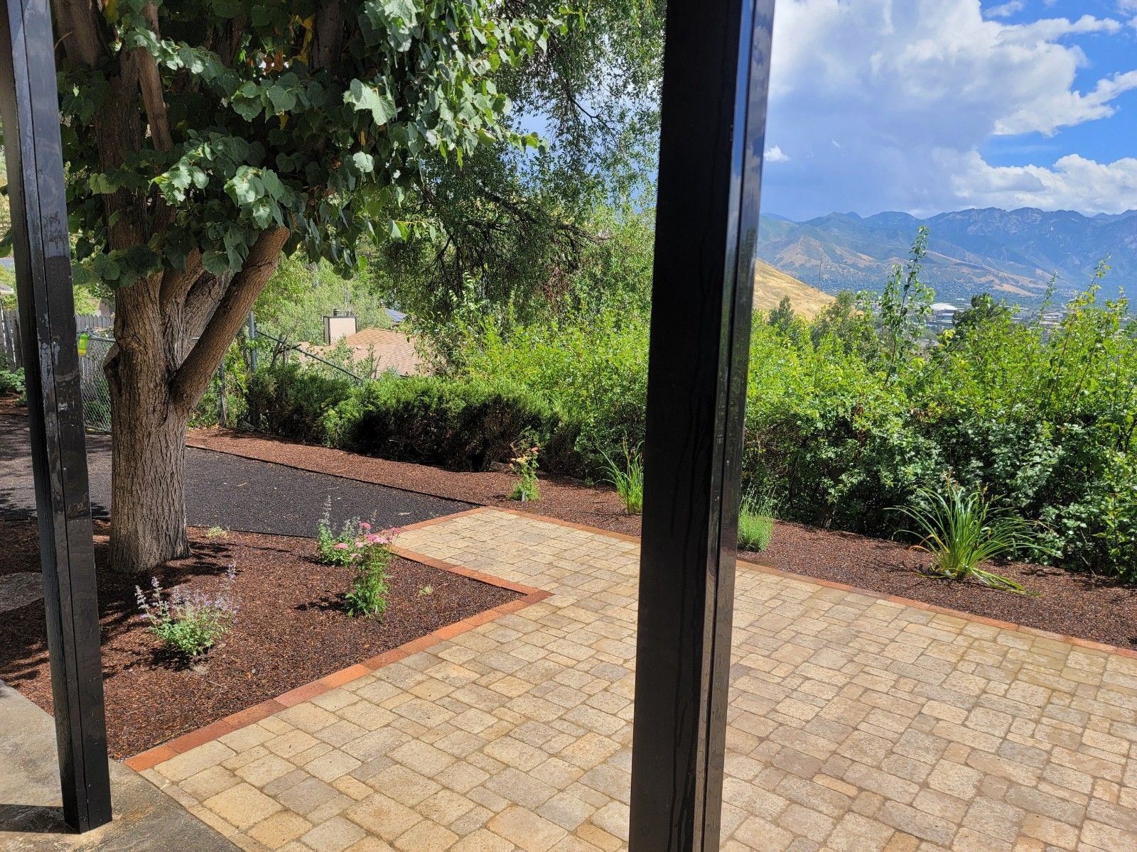 Stone patio with dark mulch and a view of green trees, hills, and sky.