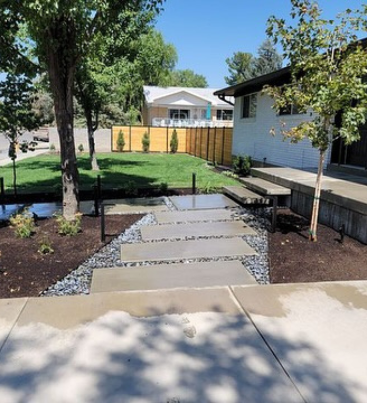 Concrete path leading to a white house with a minimalist landscaped yard and a wooden fence.