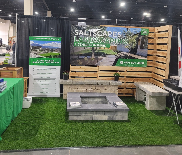 Landscape company booth with fire pit, benches, and artificial turf at an event.