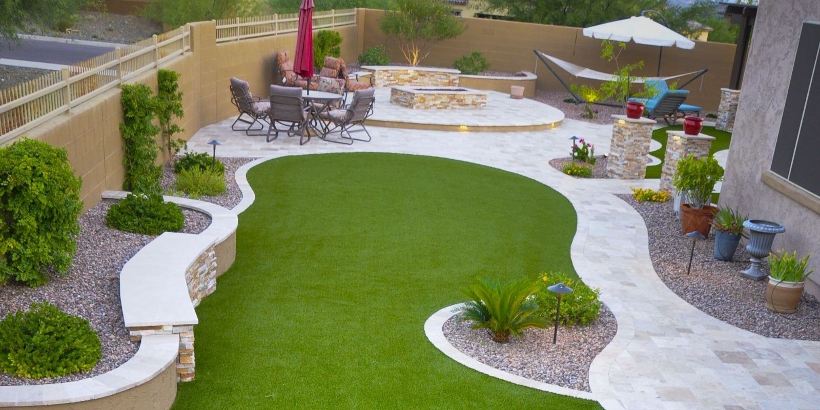 Backyard with green lawn, stone walkways, seating area with fire pit, and a hammock.