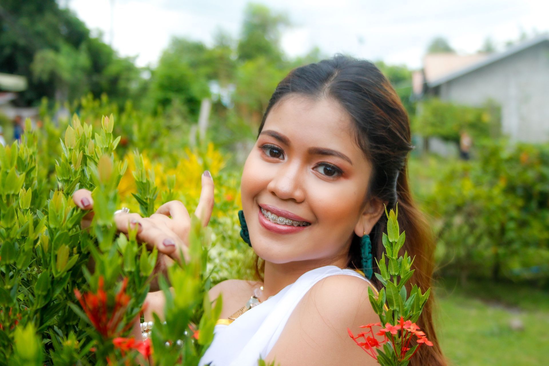 Woman standing outdoors in a garden, smiling with braces and looking at the camera