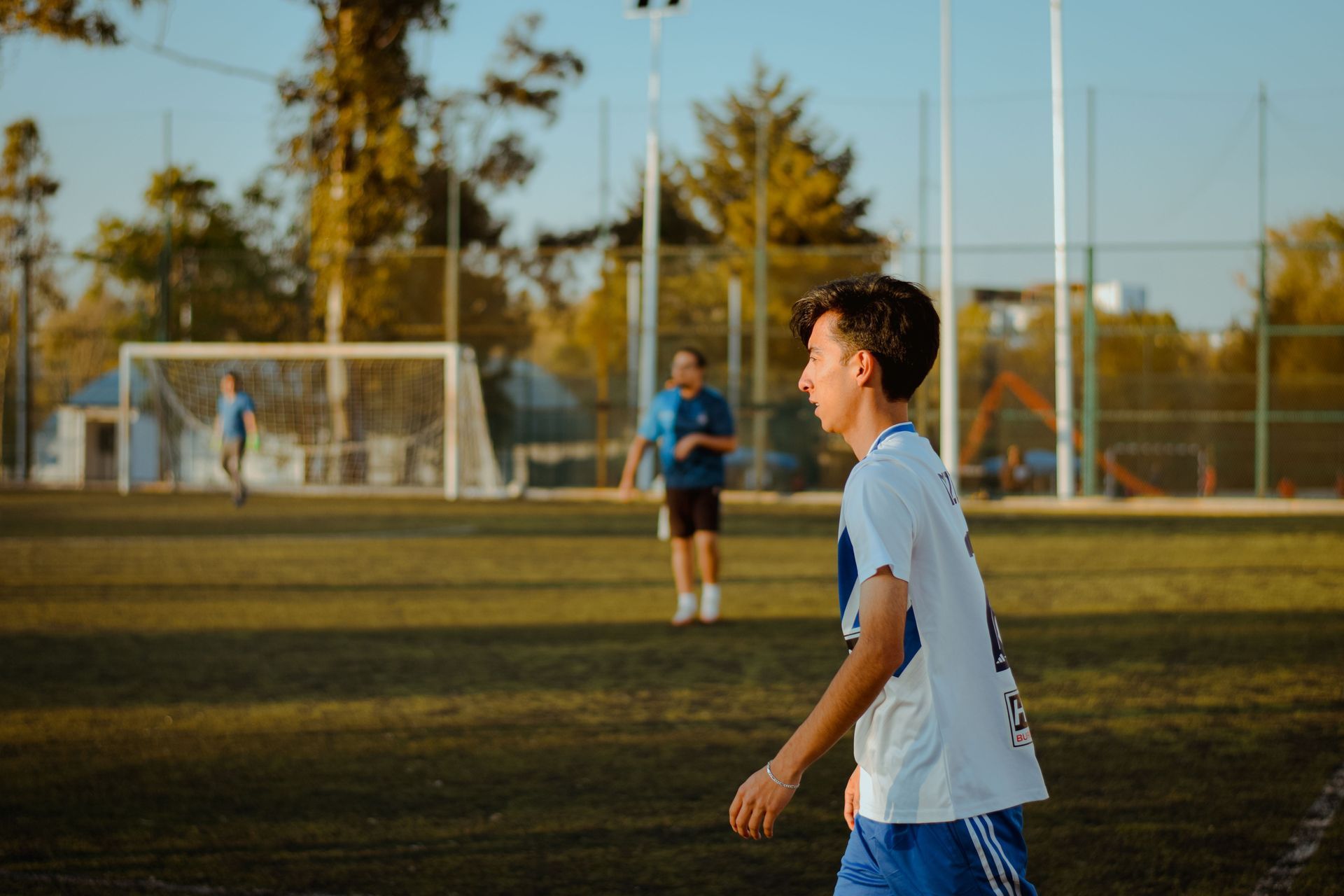 Two teenagers on opposing teams standing on a soccer pitch looking sideways towards the ball