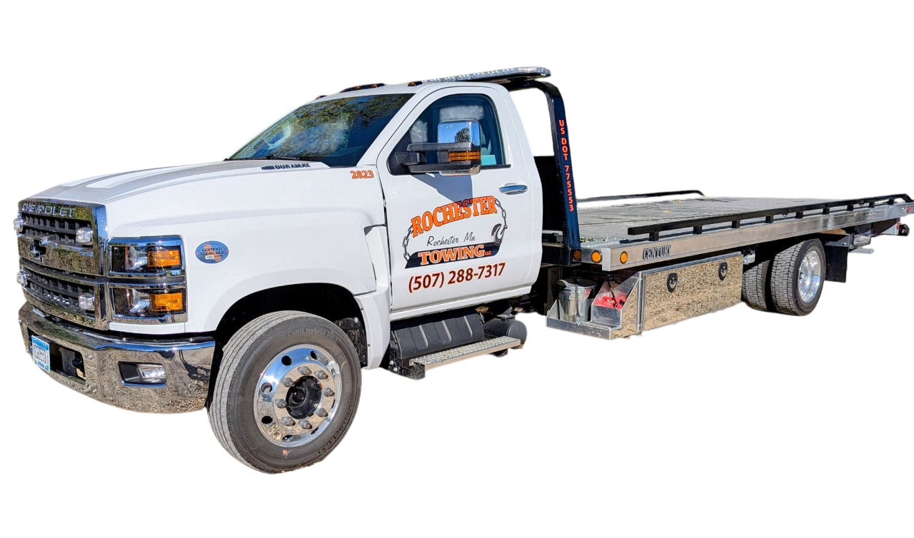 White tow truck with a flatbed on a gravel road.