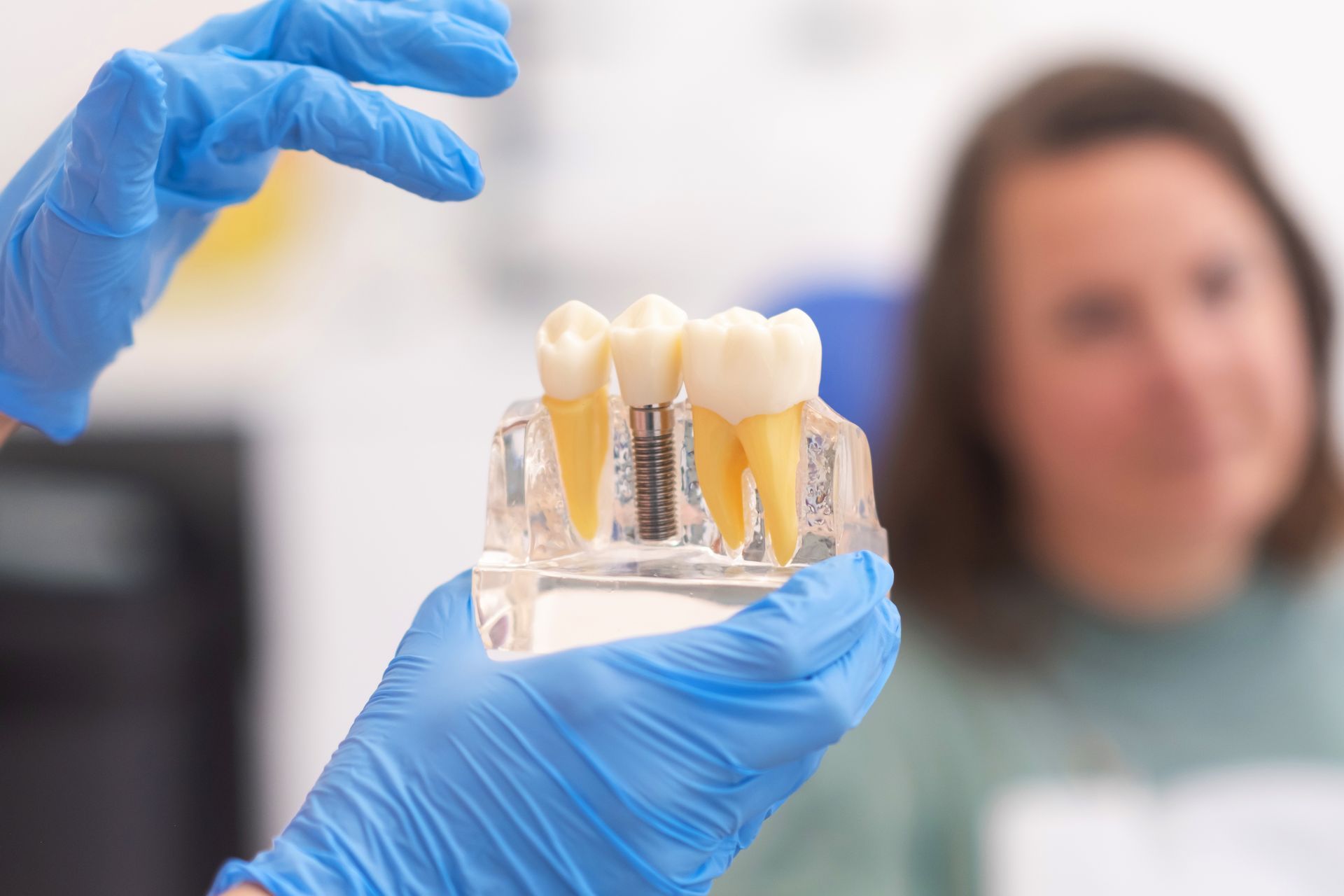 Dentist holding a dental implant model, explaining it to a patient in a dental office.