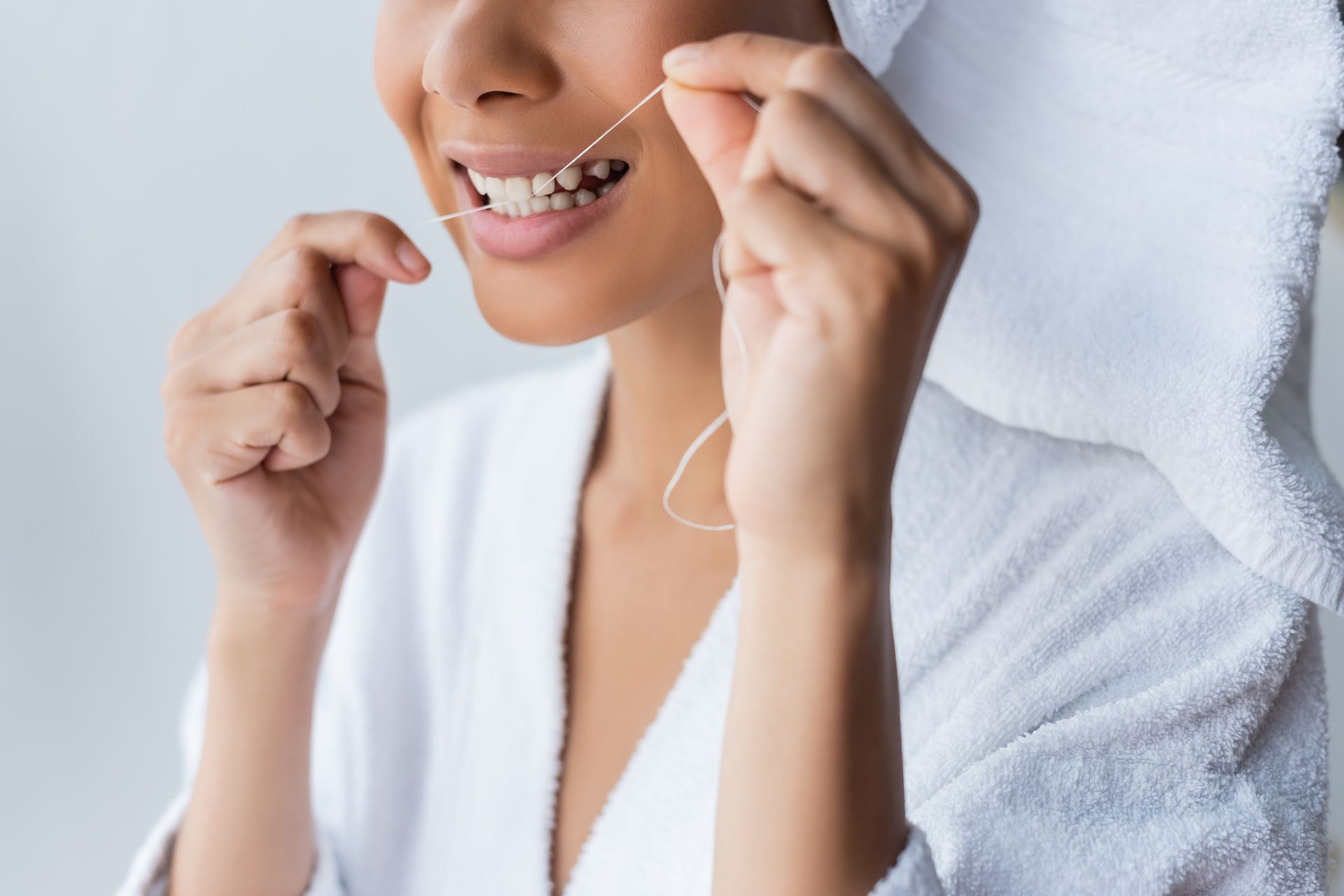 Person flossing teeth in a white robe, close-up in a bathroom