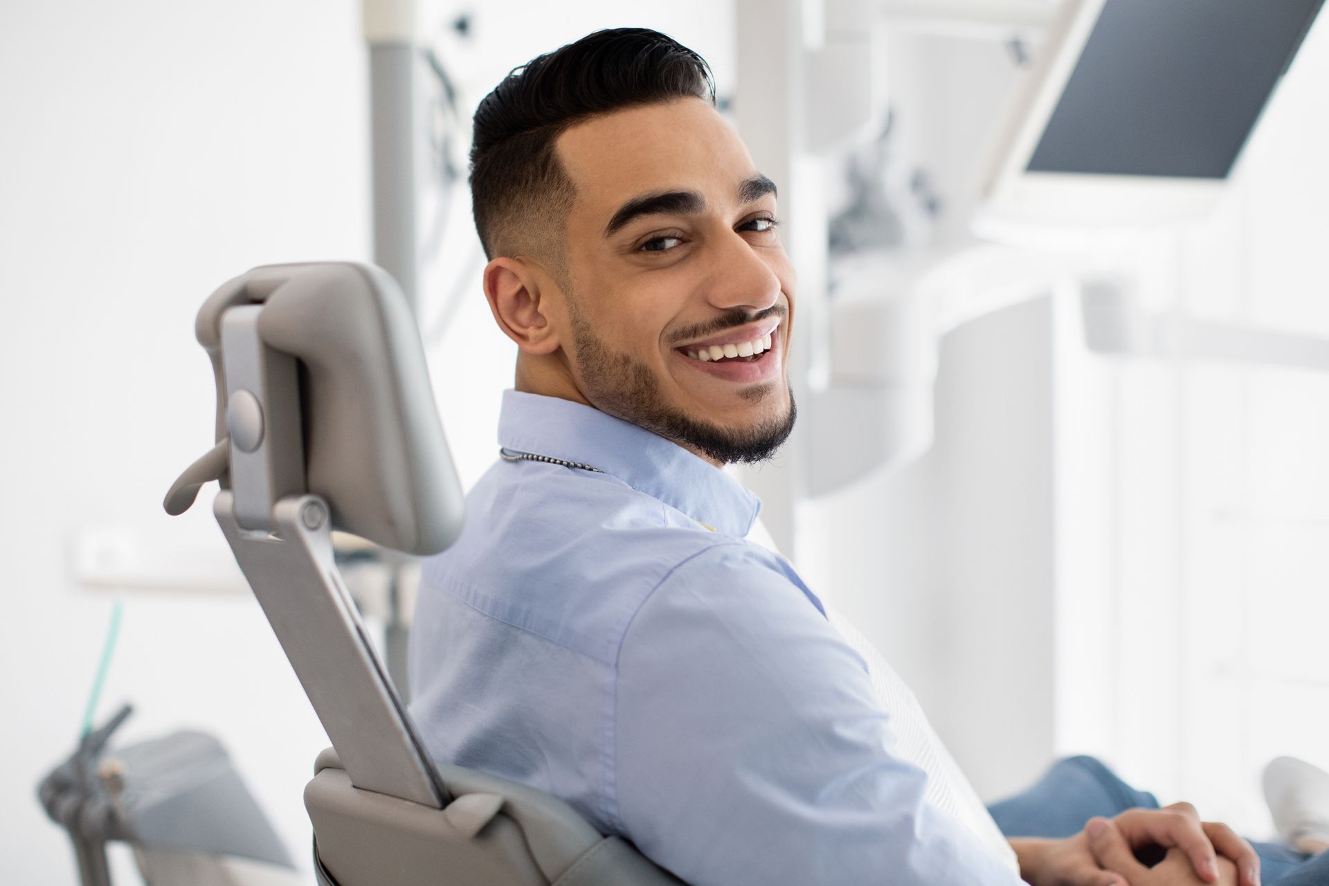 Man smiles while sitting in a dental chair. Bright, modern clinic environment.