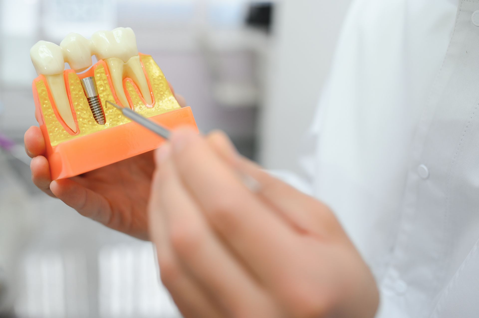 Hand holding a tooth model with dental picks in a clinic setting