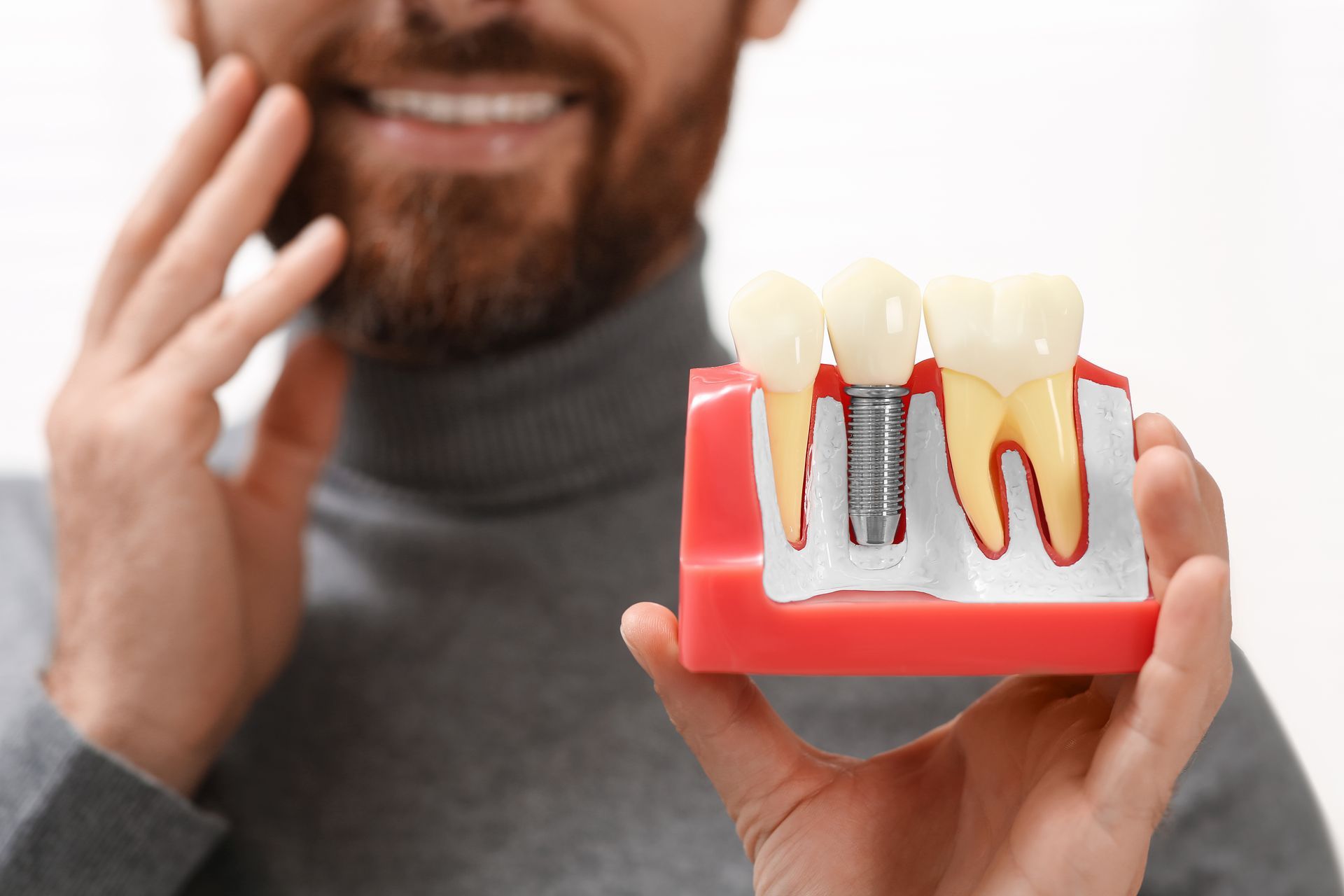 Man holding a dental implant model with red gums and white teeth, smiling in the background
