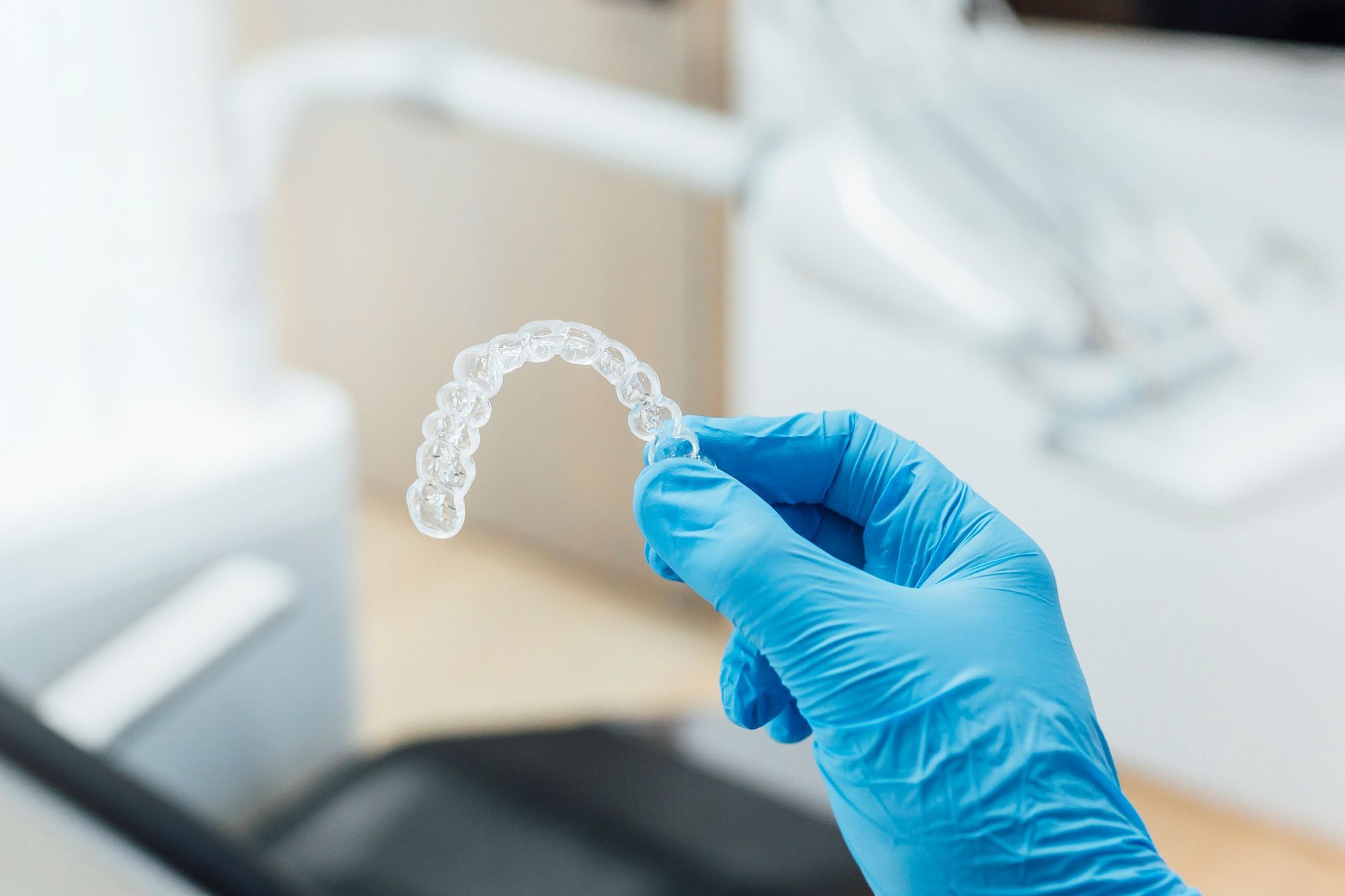 Blue-gloved hand holding a clear dental aligner in a clinical setting